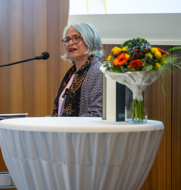 Eine Frau mit grauen schulterlangen Haaren und roter Brille steht an einem Rednerpult.