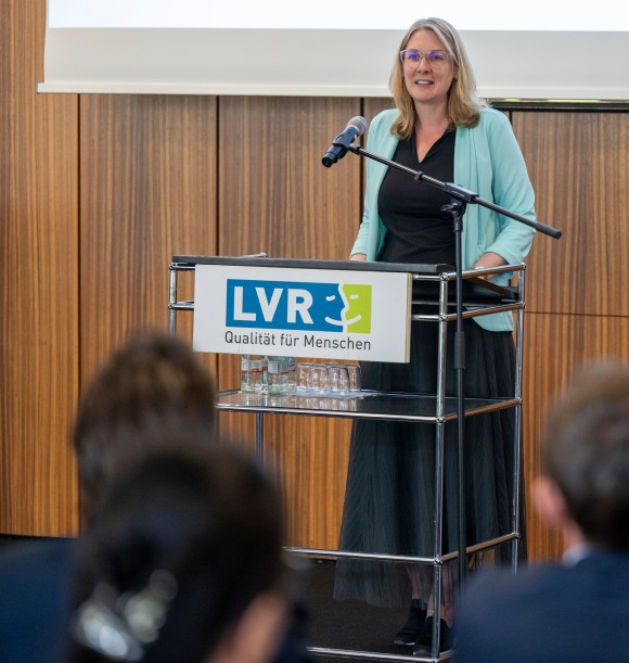 Man sieht eine Frau, die an einem Pult steht und eine Rede hält. An dem Redepult ist vorne das LVR-Log zu sehen.