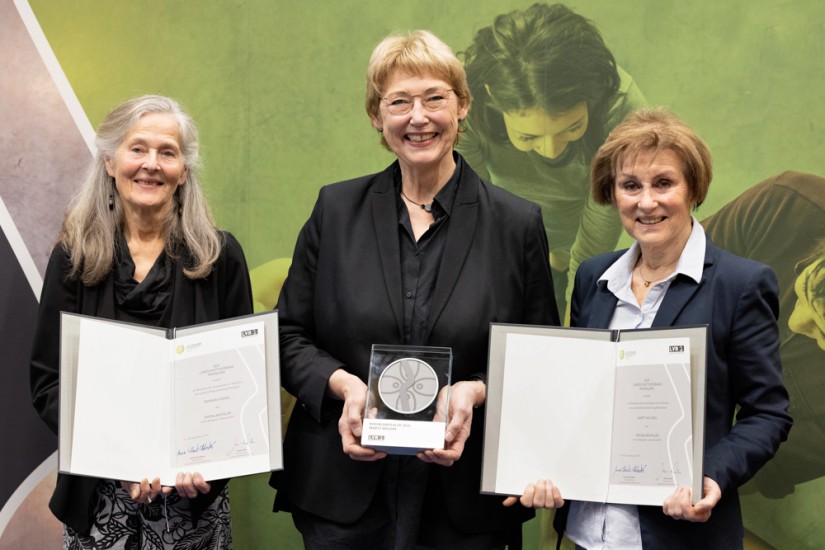 Drei Frau stehend zwei mit einer Urkunde in der Hand.