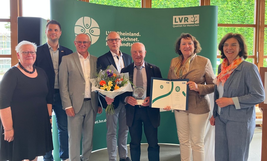 Ein Gruppenfoto mit sieben Menschen. Ein Mann in der Mitte hält eine Trophäe in der Hand.